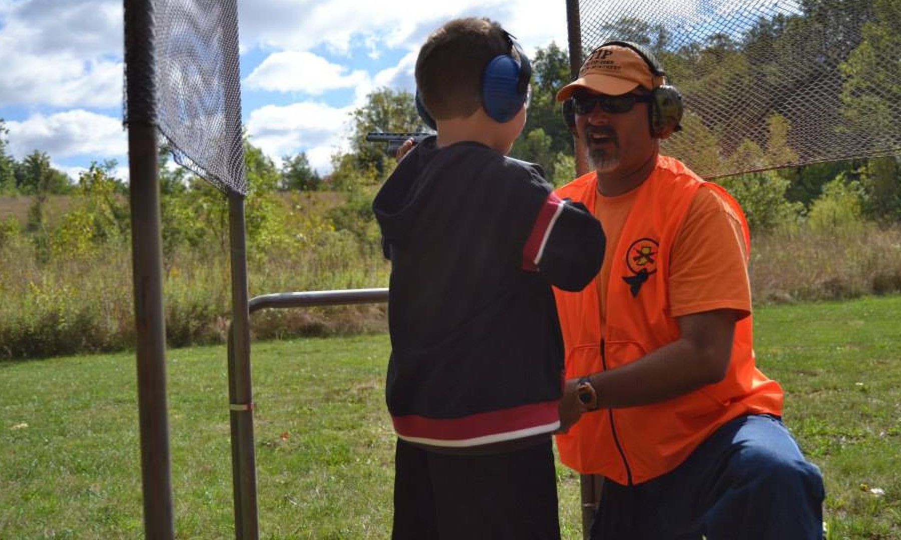 volunteer helping a youth on a outdoor shotgun range learn how to safely shoot.