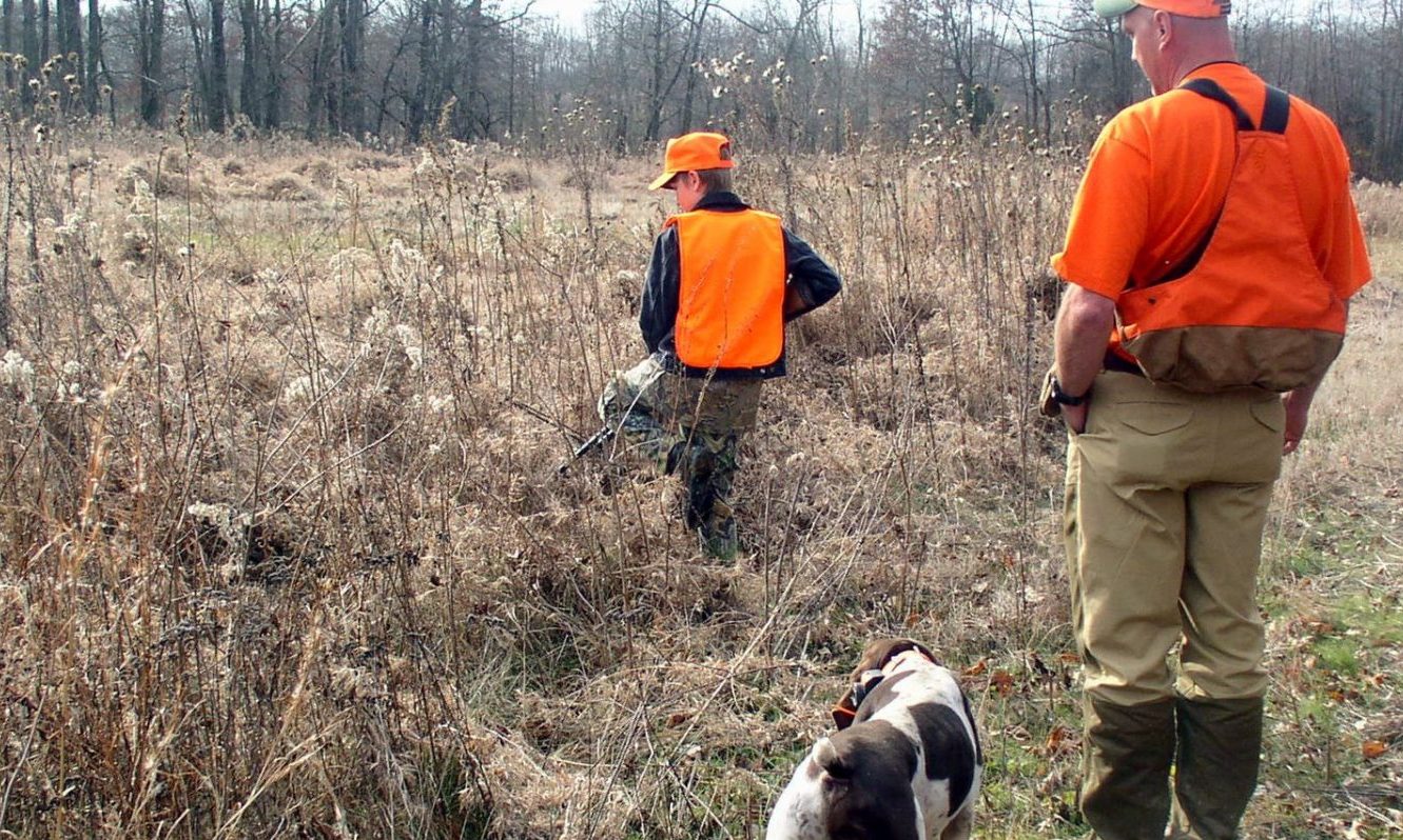 two hunters and their dog bird hunting in a field.
